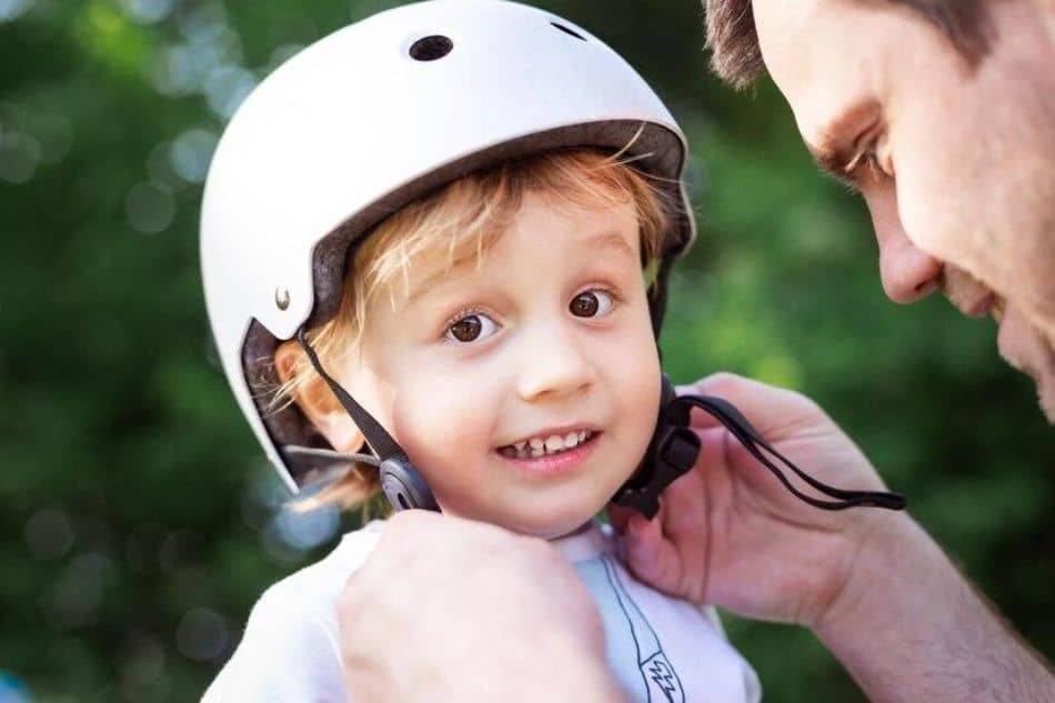 Father putting on his childs white helmet with strap