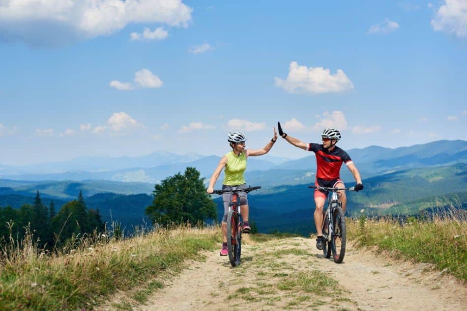 Happy couple bicyclists riding cross country bicycles on the mountain road on sunny summer day