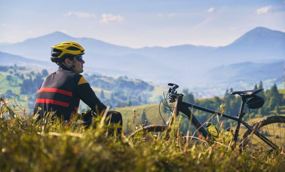 Man cyclist sitting on grass and looking at mountains