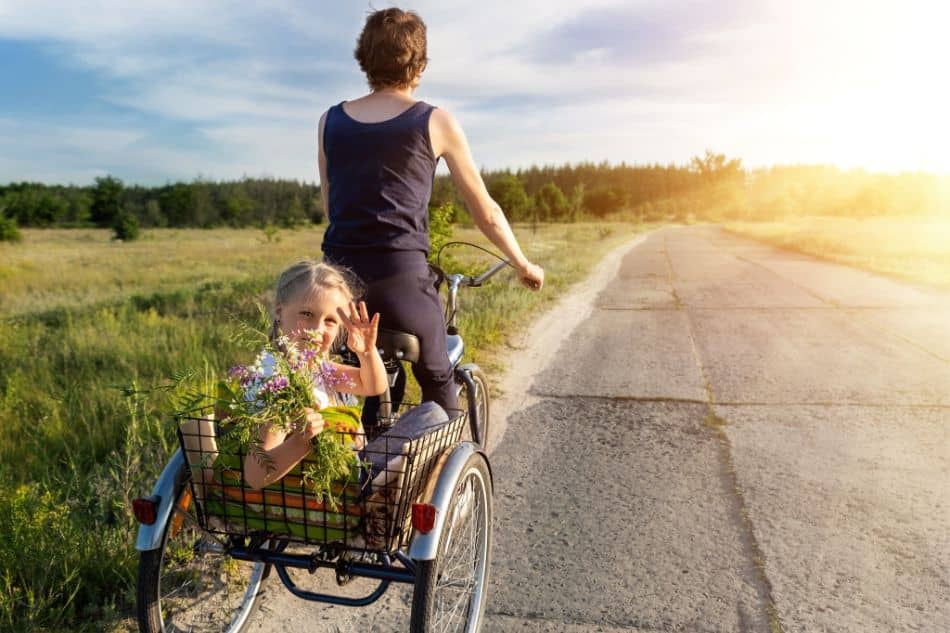 Mother and daughter riding adult upright tricycle alongside field