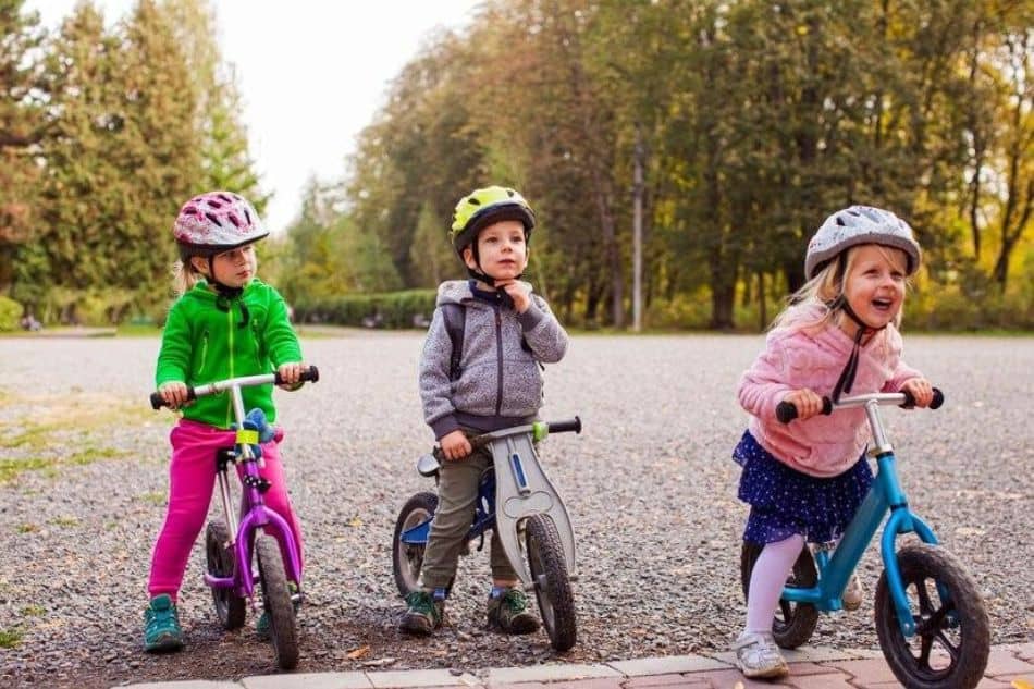 three kids riding balance bikes with buckled helmets