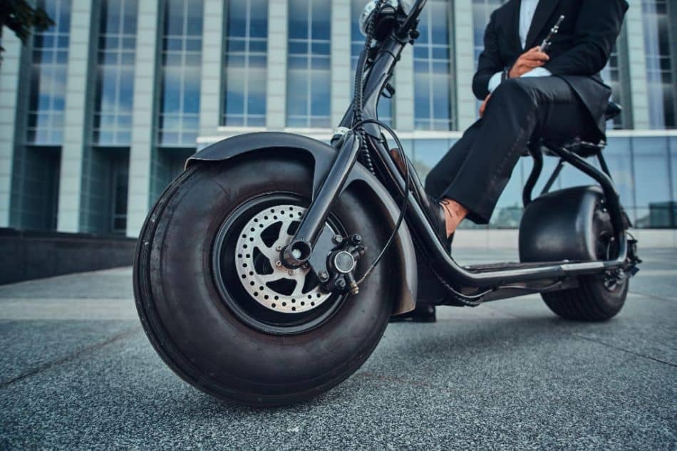 Elegant businessman in black suit is sitting on his electrical scooter near his office
