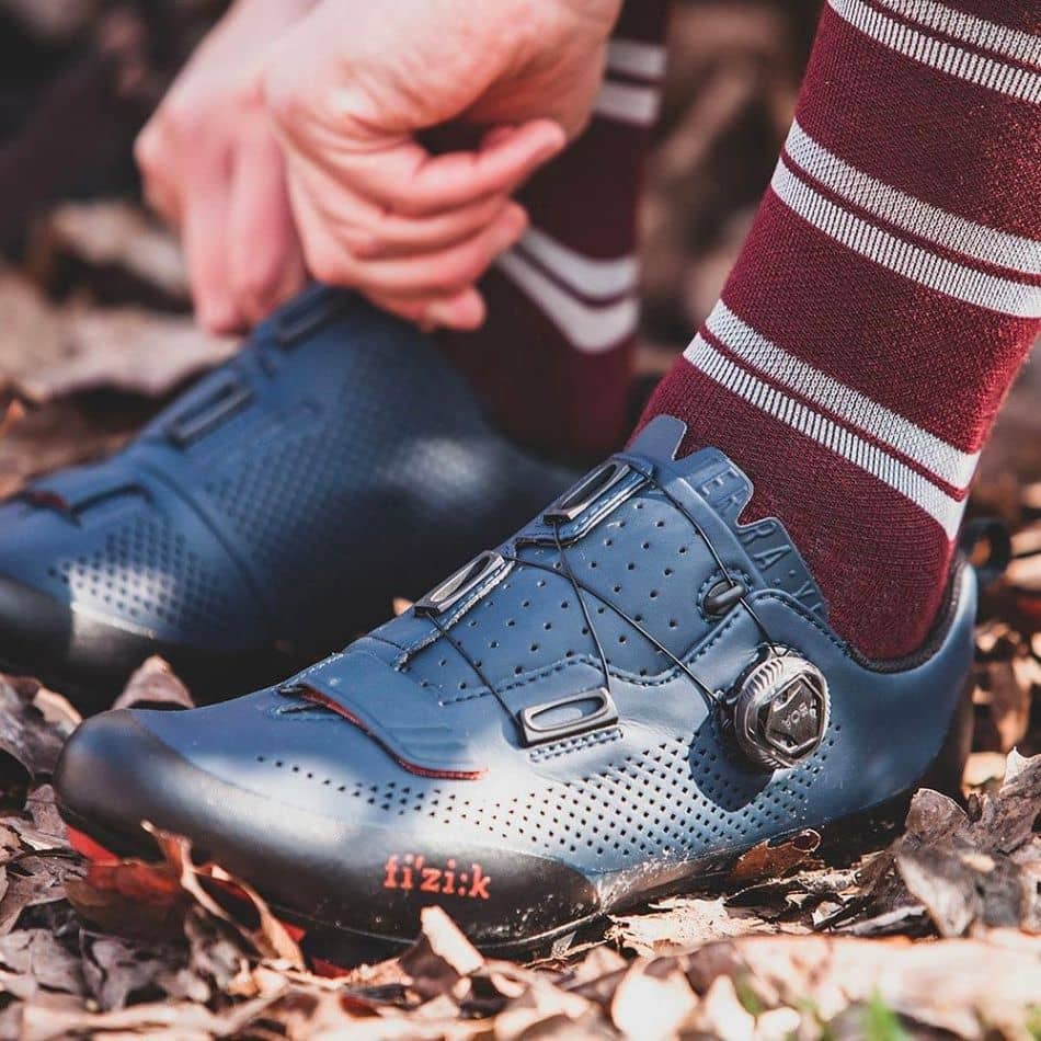 Image caption: Fizik Terra X5 women’s mountain bike shoe in leaves with red socks. Image source: Fizik.