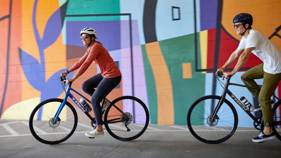 two riders on trek hybrid bicycles in front of painted mural wall
