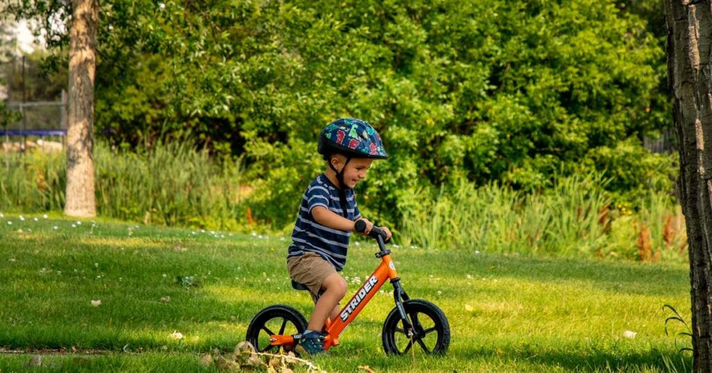 young boy riding a balance bike on path near green grass 1 1