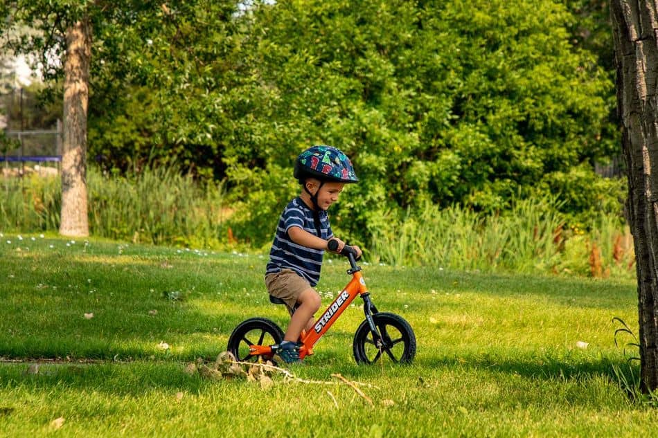young boy riding a balance bike on path near green grass 1