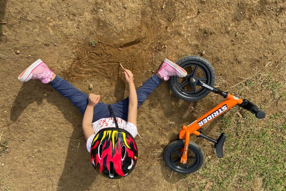 young toddler with Strider balance bike writing in the dirt 7